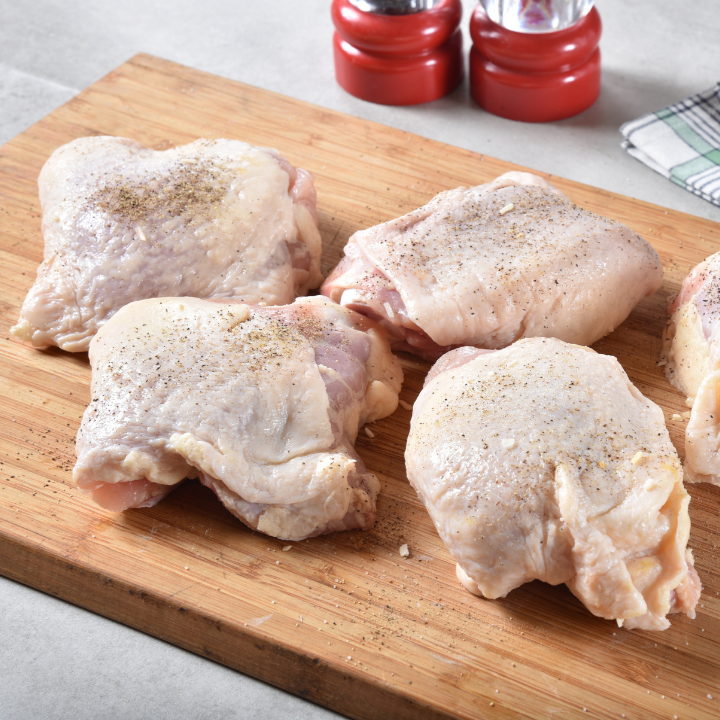 Raw chicken thighs on a wooden cutting board with seasonings in the background.