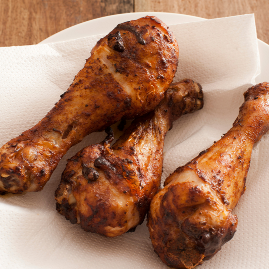 Three roasted chicken drumsticks on a paper towel with a wooden background