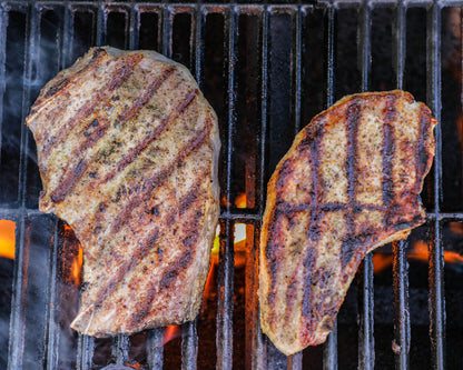 Two pieces of grilled meat on a barbecue grill with visible flames.