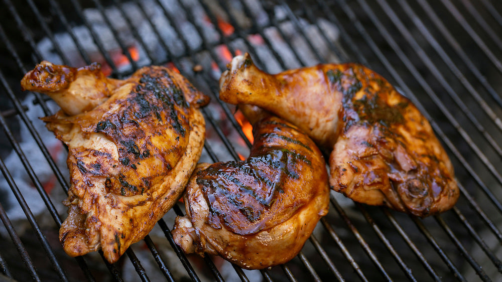 Barbecue grill with sizzling, golden-brown chicken leg quarters cooking over hot coals