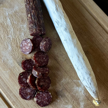 Sliced salami on a wooden cutting board with a knife.