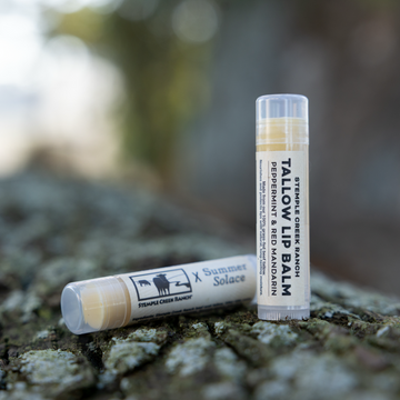 Two tubes of Tallow Balm on a textured surface with a blurred natural background